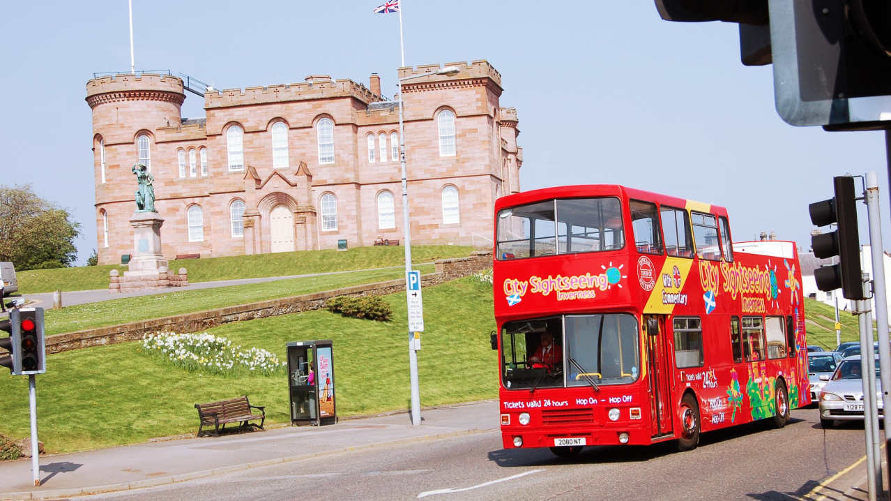 City Sightseeing Inverness Hop On Hop Off tour bus passing castle City Sightseeing Inverness Hop On Hop Off tour bus passing castle