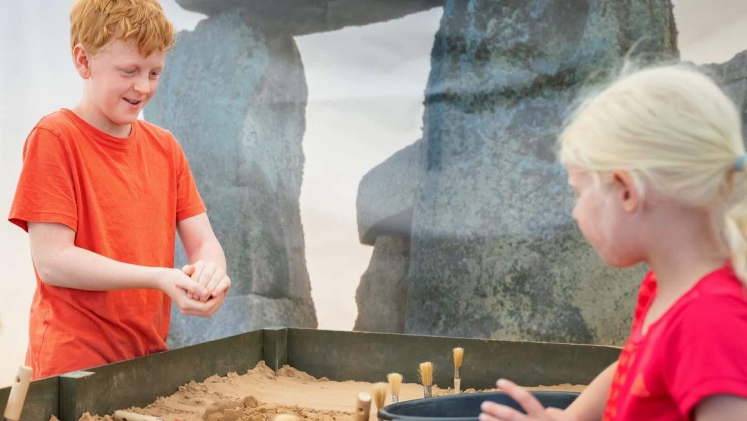 little boy in an orange top and girl in a red top are digging in the Fossil dig activity