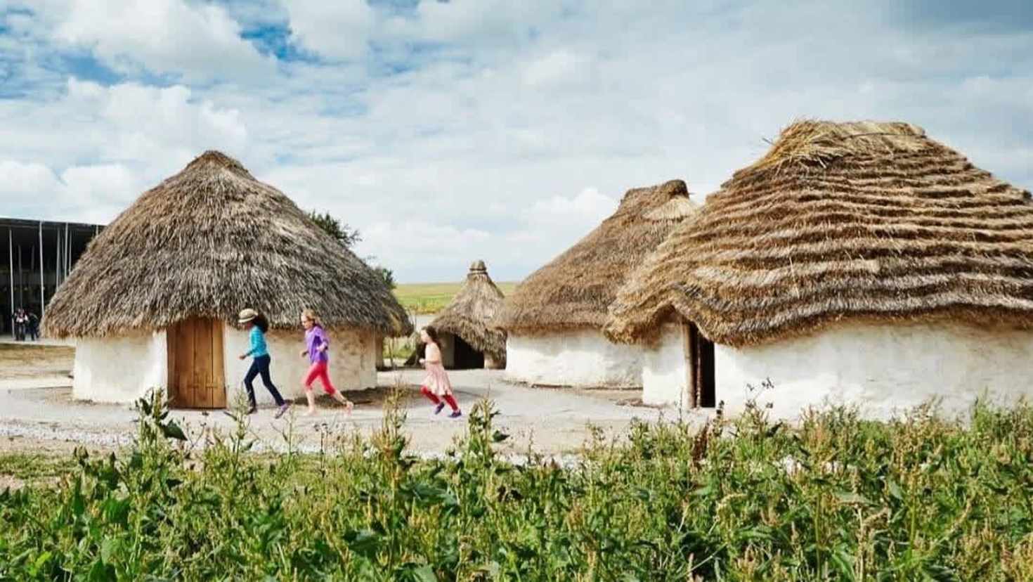children running in front of the neolithic houses.