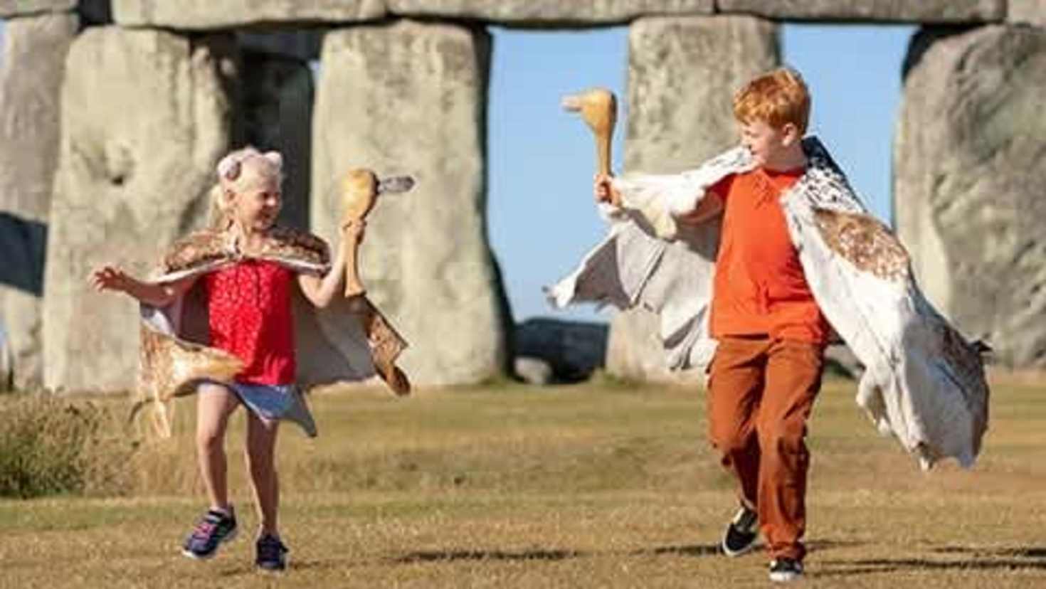 2 children wearing historical costumes running in front of the stonehenge 