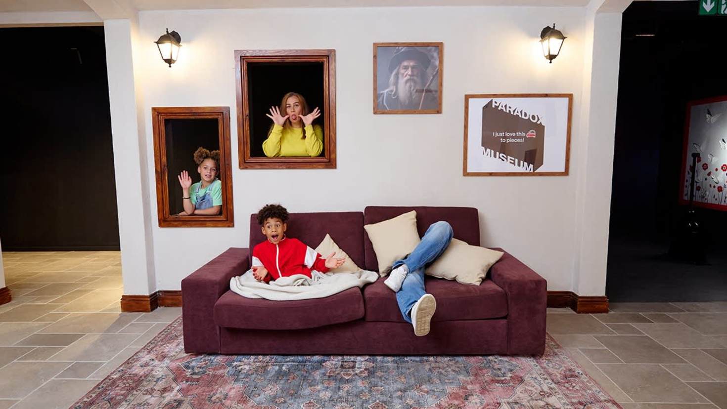 A boy lounges on a sofa while three family members pop out of picture frames in the illusion-filled Living Room exhibit at Paradox Museum London. A boy lounges on a sofa while three family members pop out of picture frames in the illusion-filled Living Room exhibit at Paradox Museum London.