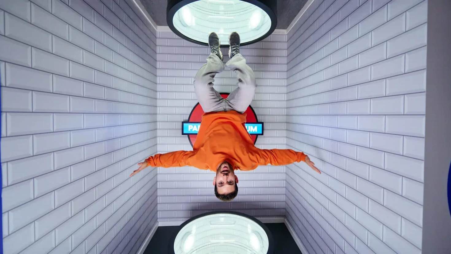 Man appearing to hang upside down in a gravity-defying illusion room styled like a tiled underground station at Paradox Museum.