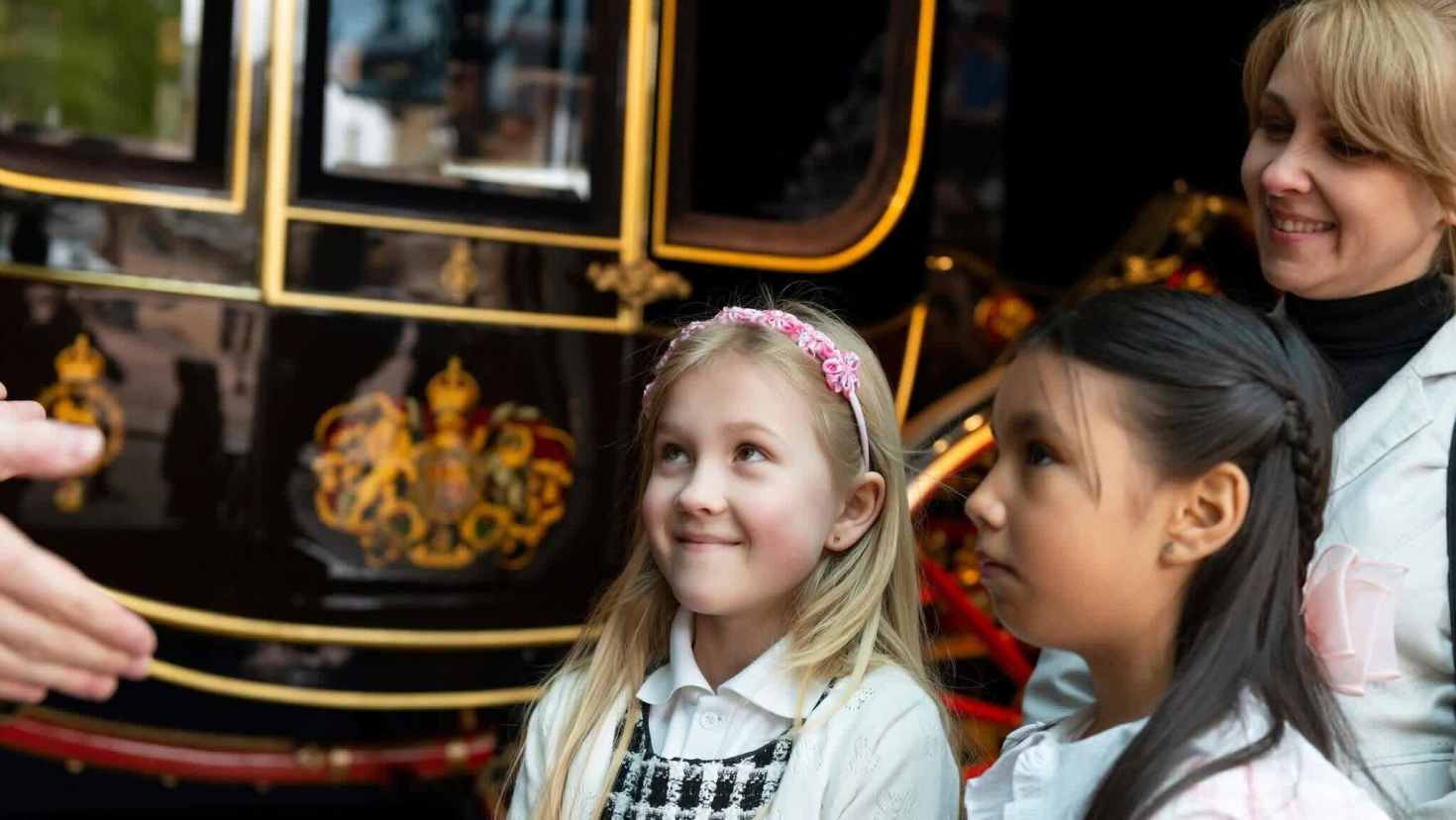 Children visiting the Royal Mews, admiring an ornate royal carriage up close during a family day out