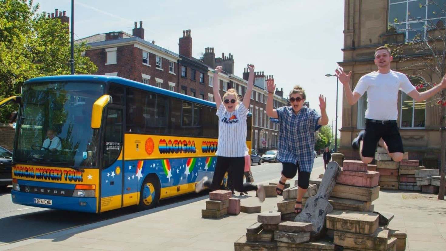 Group jumping for photos beside the Magical Mystery Tour bus in Liverpool city centre.