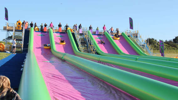 Riders sliding down bright green and pink lanes at Monster Slip and Slide Cornwall.
