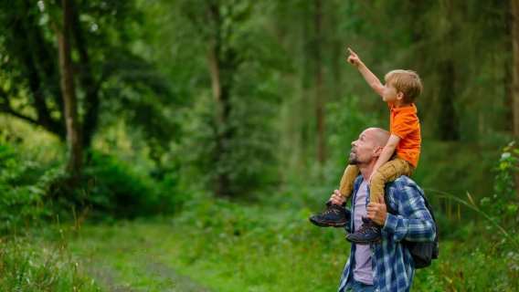 Father carrying his son through a leafy forest trail, with the child pointing out wildlife – a perfect family moment in nature.