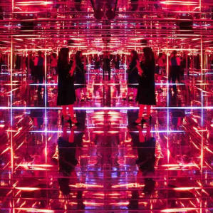 Guests walk through a neon mirror room at the Moco Museum, surrounded by glowing red and pink reflections.