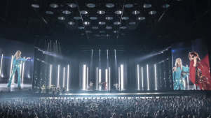 A large crowd watches the ABBA Voyage concert with digital avatars performing on a high-tech stage flanked by giant video screens.