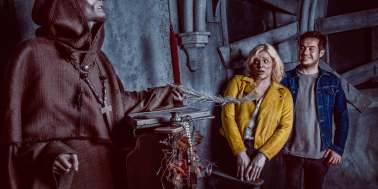 Scared girl in a yellow jacket and smiling man interacting with a scary priest at York Dungeon 