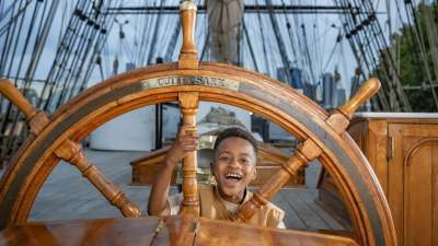 Young boy smiling at the Cutty Sark ship’s wheel on the historic deck in Greenwich