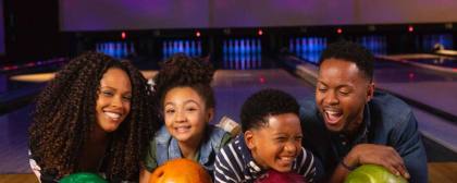 family holding bowling balls and smiling