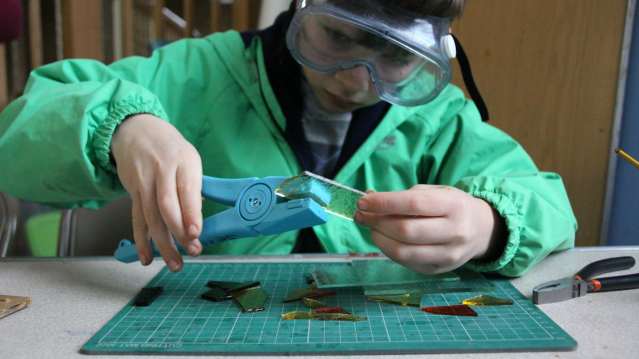 A kid touches stained glass through gloves at the stained glass museum