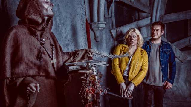 Scared girl in a yellow jacket and smiling man interacting with a scary priest at York Dungeon 