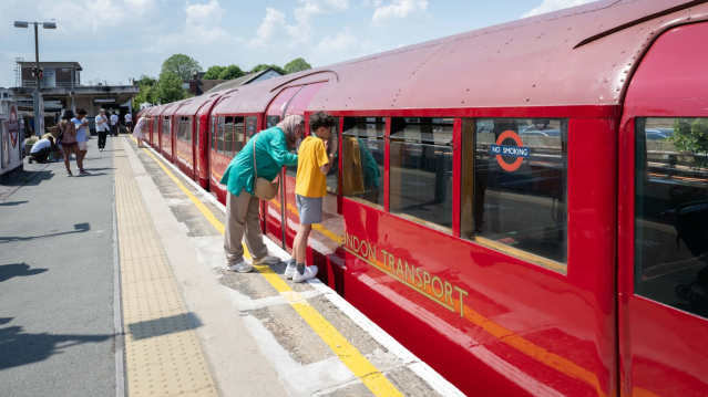 Family looking inside a historic red London Underground train at London Transport Museum.