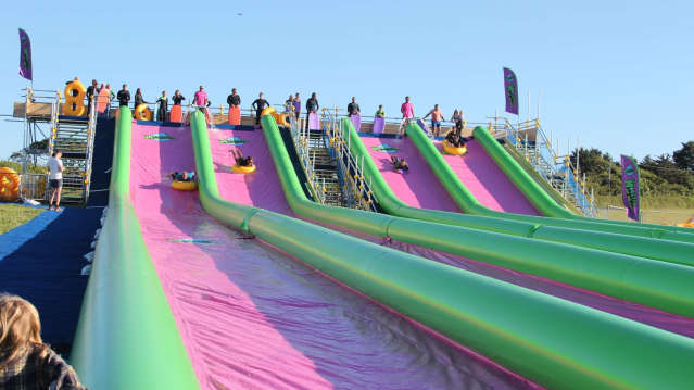Riders sliding down bright green and pink lanes at Monster Slip and Slide Cornwall.