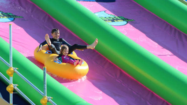 Siblings sliding on inflatable ring down green and pink lanes at Monster Slip and Slide Cornwall.