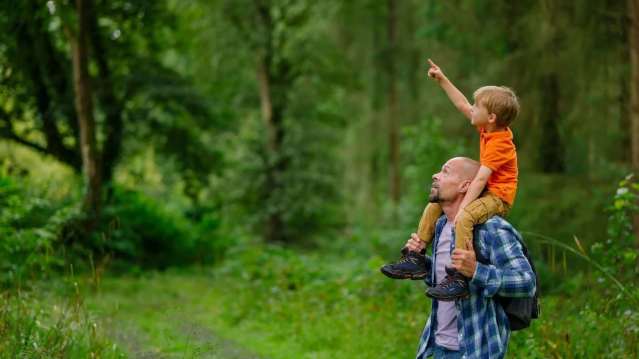 Father carrying his son through a leafy forest trail, with the child pointing out wildlife – a perfect family moment in nature.