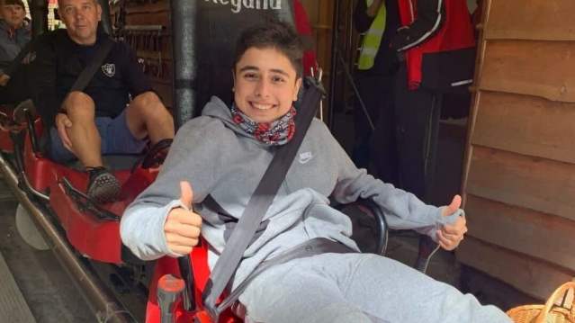 Smiling teens in a red alpine coaster ready for their ride inside a wooden station at a forest park.