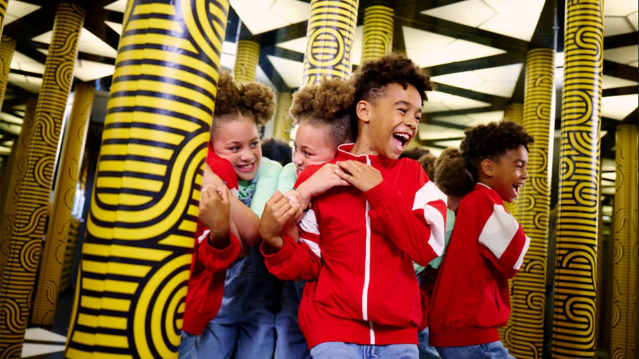 Group of children laughing and playing in a mirrored maze room with bold yellow patterned pillars at Paradox Museum.