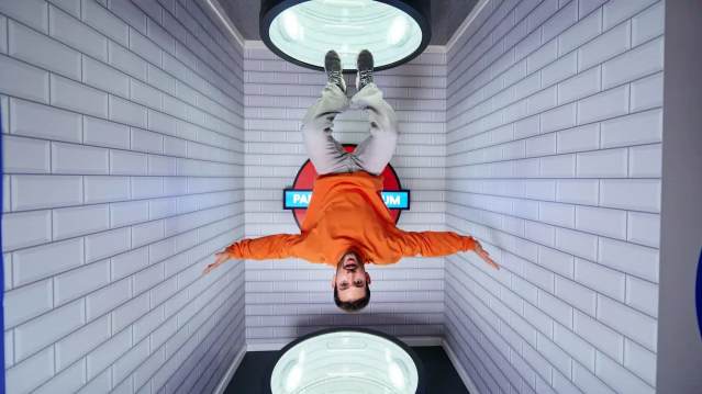 Man appearing to hang upside down in a gravity-defying illusion room styled like a tiled underground station at Paradox Museum.