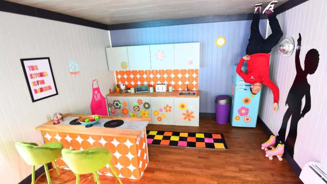 Retro upside‑down kitchen scene at Upside Down House Liverpool with guest posing on ceiling