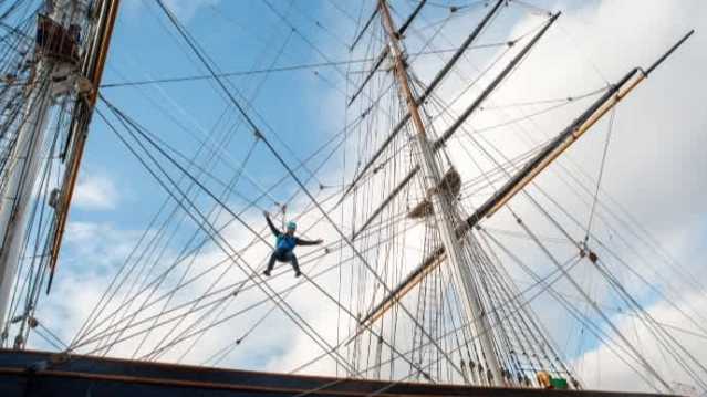 Cutty Sark rig climb participant suspended on ship’s rigging against bright blue sky
