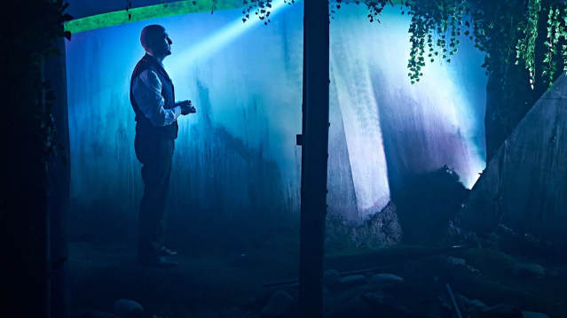 Performer stands in atmospheric blue lighting during a scene in Jeff Wayne’s War of the Worlds immersive show, available with Jeff Wayne’s War of the Worlds tickets.