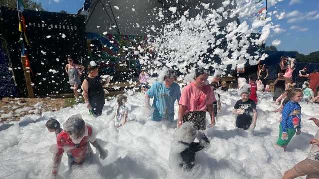 Children and adults playing in a large foam party with bubbles covering the ground.